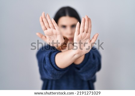 Young brunette woman standing over isolated background rejection expression crossing arms and palms doing negative sign, angry face 