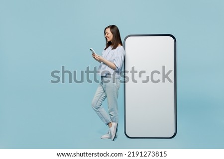Full body young happy woman she 20s in casual blouse big huge blank screen mobile cell phone with workspace copy space mockup area hold smartphone isolated on pastel plain light blue background studio Royalty-Free Stock Photo #2191273815