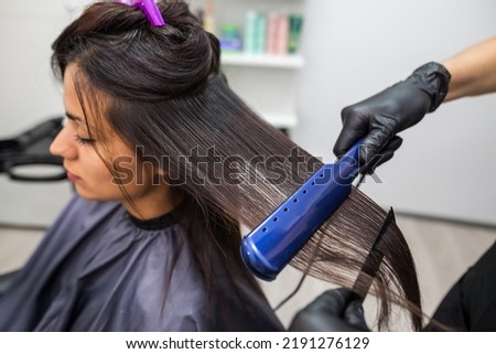 Hairdresser using a hair straightened to straighten the hair. Hair stylist working on a woman's hair style at salon. Royalty-Free Stock Photo #2191276129