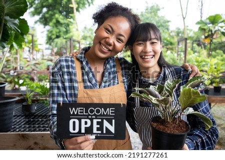 African American woman owner an ornamental garden with assistant using chart board to check the plants on a shelf in a green house for sell. Portrait of charming woman owner. Welcome we are OPEN.