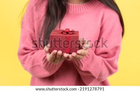 Portrait of a smiling happy beautiful Asian woman holding a small gift box in hand. Studio photography isolated on pink background. Birthday, New Year, Christmas, Holiday concept.