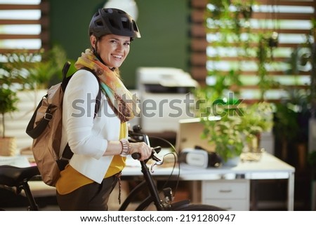 Portrait of smiling trendy middle aged business woman in bike helmet with bicycle and backpack in modern eco office. Royalty-Free Stock Photo #2191280947