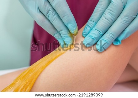 Woman undergoing leg hair removal procedure with sugaring paste in salon. Skin care, remove hair with sugar paste
