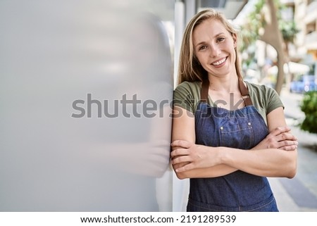 Young blonde woman smiling happy wearing apron at street