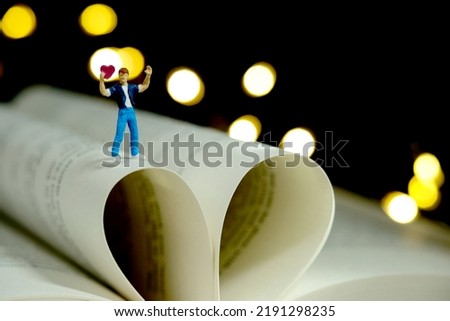 Miniature people toy photography. Poem and poetry concept. Boy standing above opened book, express his love holding heart shape. Romantic bokeh light background. Image photo