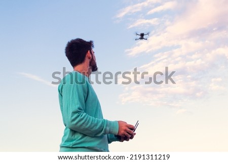white, slim, attractive, young man controlling a modern drone at sunset, back view