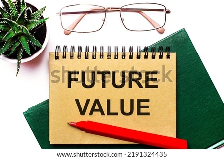 On a light background, gold-framed glasses, a flower in a pot, a green notebook, a red pen and a brown notebook with the text FUTURE VALUE. Business concept