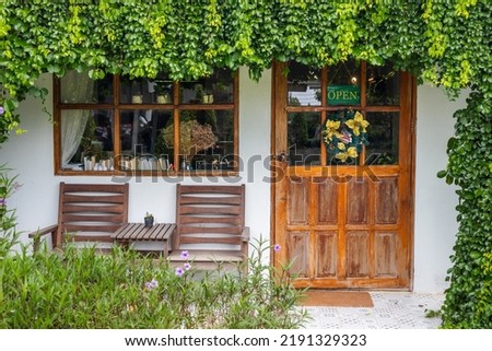 The door in front of the café and an open sign covered by plants and flowers.