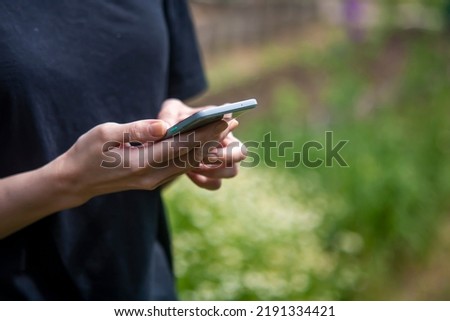 Holds a phone or device in his hands. Against the background of green vegetation.