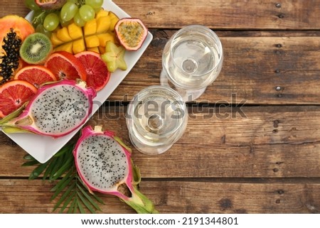 Delicious exotic fruits and wine on wooden table, flat lay