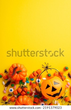 Halloween concept. Top view vertical photo of pumpkin basket for trick-or-treat spooky eyes candies with insects cockroach centipedes and spiders on isolated yellow background with copyspace