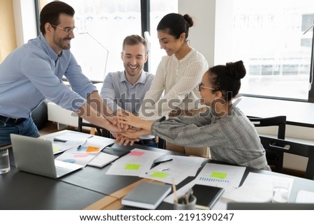 Motivated young mixed race teammates putting hands together, feeling power of collaboration starting new workday or developing project together at brainstorming meeting in modern boardroom office. Royalty-Free Stock Photo #2191390247