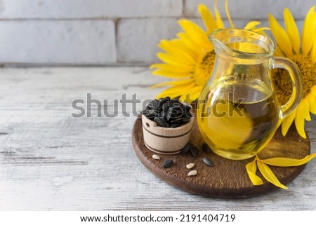 Glass jar with oil, wooden bowl full of ripe sunflower seed and two sunflowers on the wooden round kitchen board on the rustic background. Copy space