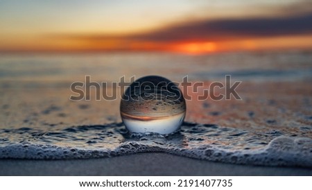 Photo of a sphere at the edge of the ocean water with sunset light.
