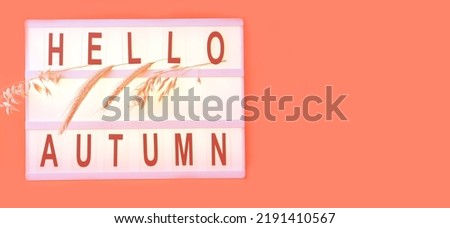 Light box with word HELLO AUTUMN and ears of wheat on Coral color background. Creative composition for seasonal projects and basis designs. Close-up 