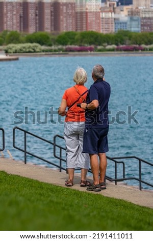 An older white couple taking picture of the Chicago skyline standing in front of the water at Lake Michigan in Illinois.