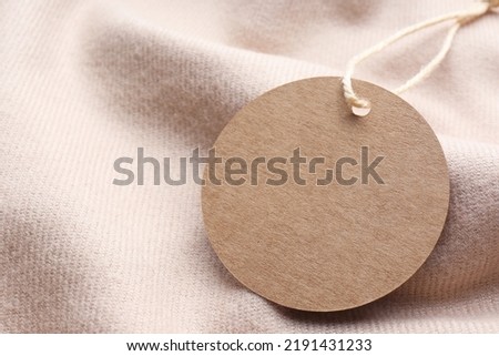 Circle shaped tag with space for text on beige fabric, closeup