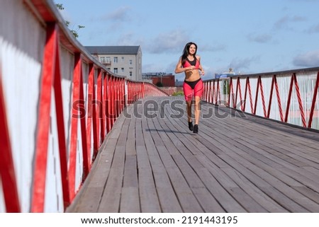 A woman in a pink sweat suit runs across the bridge. Royalty-Free Stock Photo #2191443195