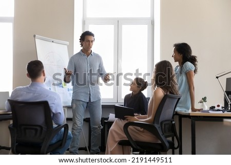 Hispanic businessman, project leader makes motivational speech to corporate staff members, give presentation on flip chart during group meeting or educational seminar, business training event Royalty-Free Stock Photo #2191449511