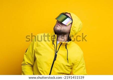 Young man in cyberpunk glasses in a yellow jacket looks up on a yellow background.