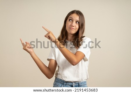 Happy beautiful teenage european girl smiling and pointing fingers aside isolated over beige background. Copy space
