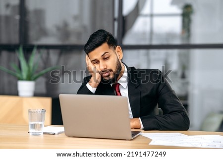 Fatigue, chronic sleep deprivation. Sleepy arabian or indian business man in a suit, sit at workplace in office with a laptop, put his head on his hand, fell asleep during work, feels tired Royalty-Free Stock Photo #2191477249