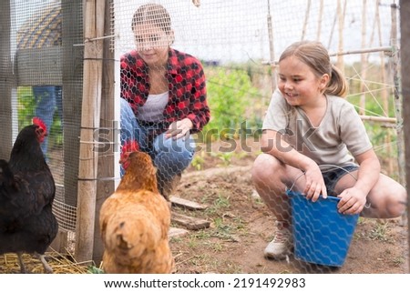 Smiling young woman with little girl feeding poultry in aviary at allotment Royalty-Free Stock Photo #2191492983