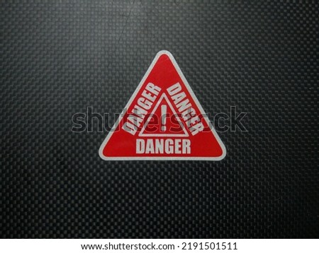 Red danger sign on black carbon background.