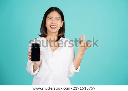 Excited young asian woman standing hold mobile cell phone with blank empty screen spreading hands isolated on bright green background, studio portrait