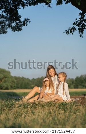 Mother and daughters relax in nature. Vertical photo of a mother with children. Family photo shoot in the village in the field. Psychology of the relationship between mother and child