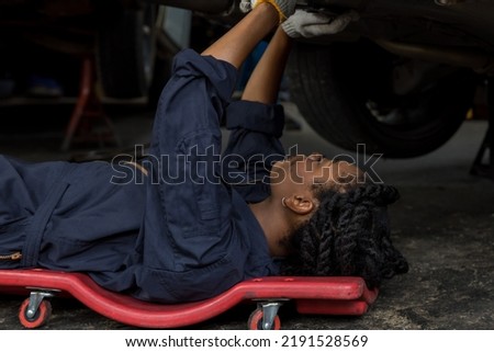 Mechanic lying down and working under car at auto service garage. Technician vehicle maintenance and checking under car at automotive motor garage. Royalty-Free Stock Photo #2191528569