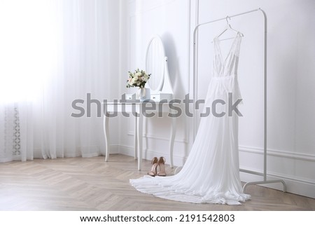 Elegant wedding dress hanging on rack indoors Royalty-Free Stock Photo #2191542803