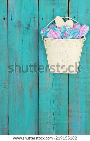 Tin pot of country hearts hanging on antique teal blue distressed wood fence