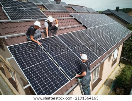 Men installers mounting photovoltaic solar moduls on roof of house. Engineers in helmets installing solar panel system outdoors. Concept of alternative and renewable energy. Aerial view. Royalty-Free Stock Photo #2191564163