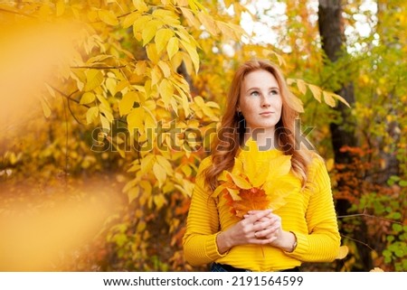 Autumn. red-haired girl in a yellow sweater holds a bouquet of autumn leaves in her hands. Warm tones. Orange. A place for text. High quality photo