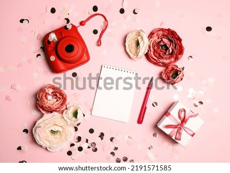 Modern instant camera with blank notepad, flowers and gift box on pastel confetti pink background. Flat lay, top view, copy space.