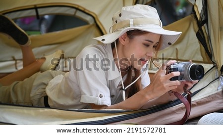 Asian female traveler lying inside camp tent and checking picture in camera. Adventure, leisure, vacation and camping concept