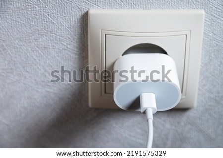 Electric socket on a pink wall. The black wire plug is connected. Renovated backdrop of studio apartment. Blank copy space single white plastic socket