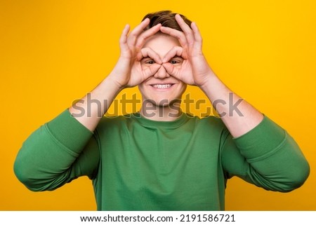 Portrait of happy man looking at camera through fingers okay signals over vibrant shine color background.