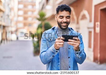 Young hispanic man watching video on smartphone at street Royalty-Free Stock Photo #2191600137