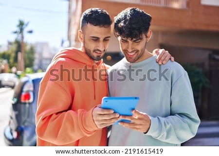 Two man couple hugging each other using touchpad at street