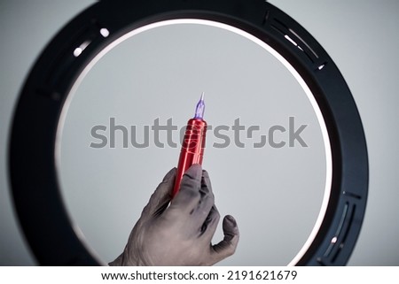 A machine for permanent makeup on grey background closeup. Permanent machine in hand, Cosmetic Tattoo tool, ring light