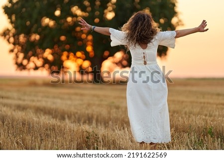 Curly haired caucasian woman in a harvested wheat field at sunset, portrait with selective focus