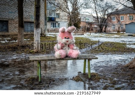 Pink plush rabbit sits on a bench in a poor residential area. Bad weather. Depression. Sadness. Love