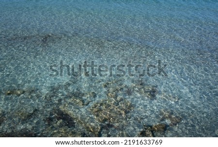 Background and texture of blue water with small waves. The water is clear and transparent. Below you can see sand and rocks.