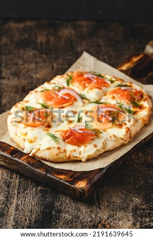 Roman pizza with salmon served on wooden board. Traditional roman pizza with fish. Roman square pizza or Pinsa on thick dough, Italian Cuisine.