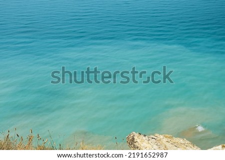 Blurred background, view of the sea in the midday heat from the rocky shore. Hot summer vacation, pastel colors and reflections on the water. Abstract blur poster or advertising banner