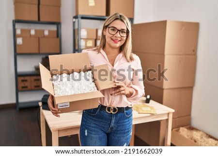 Young hispanic woman ecommerce business worker holding open package at office