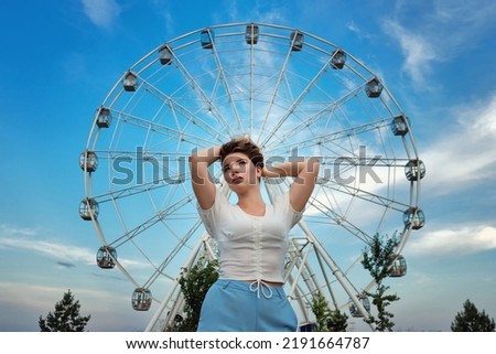 Young woman posing in city park near Ferris wheel. 