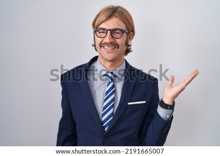 Caucasian man with mustache wearing business clothes smiling cheerful presenting and pointing with palm of hand looking at the camera. 